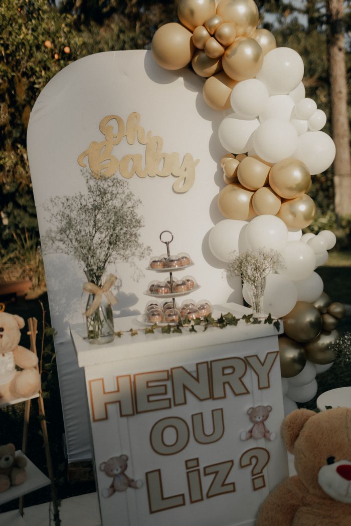 about-img Elegant gender reveal setup with gold and white balloons and teddy bears outdoors.