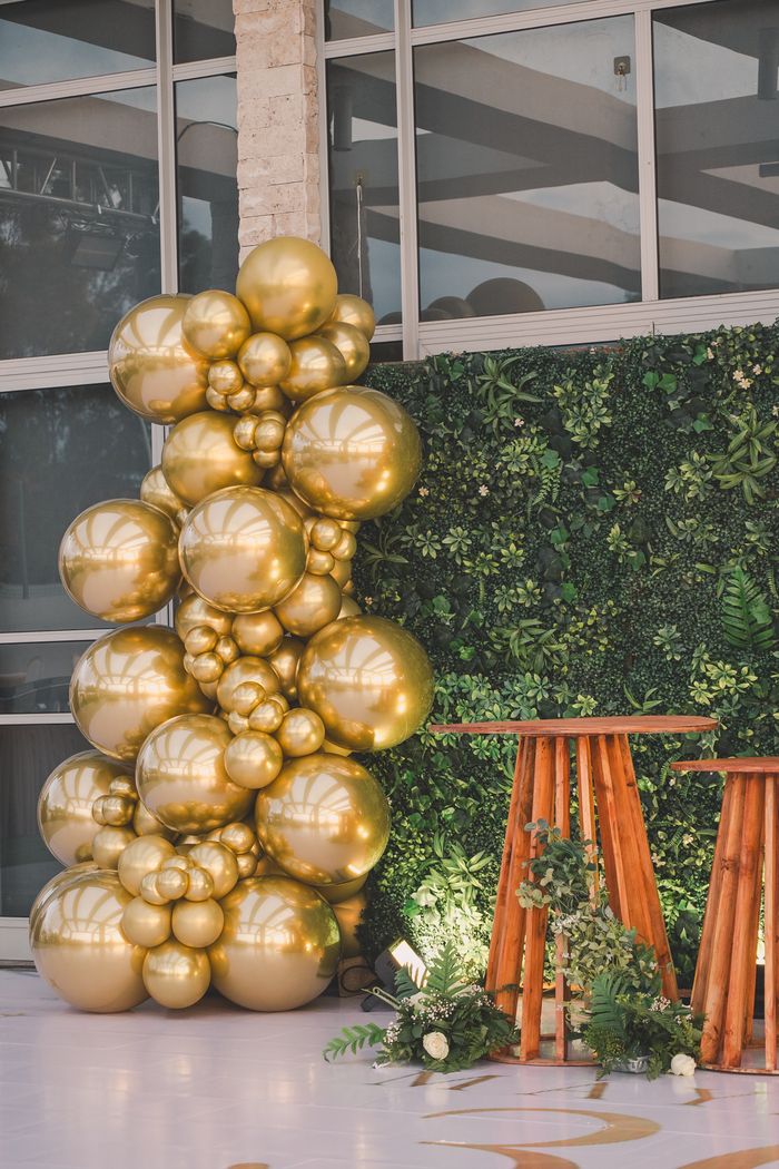 Gold balloon arrangement against a lush green wall, perfect for events.